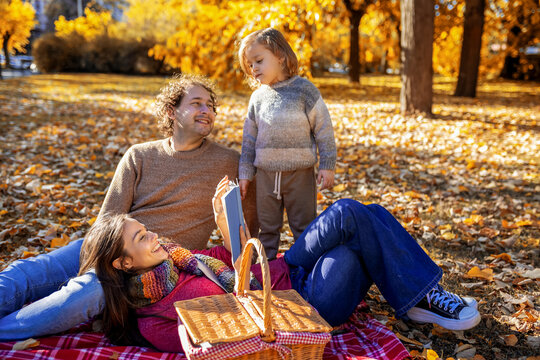 Little boy standing by parents on autumn picnic blanket