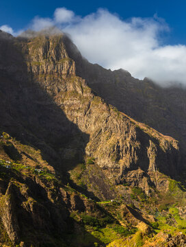 View of the rugged mountain landscape of Santo Antao with steep rocky cliffs, lush green vegetation, and dramatic shadows in Faja de Cima, Paul, Cabo Verde.