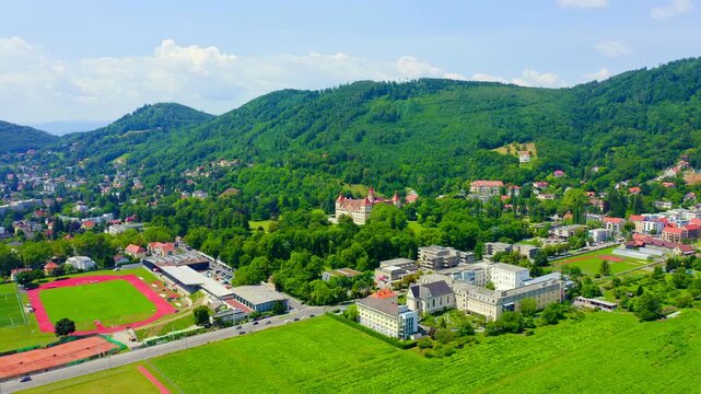 Graz, Austria. Eggenberg Palace, a Baroque residence with red-tiled towers and symmetrical wings, Drone footage over green parkland and the Plabutsch hillside. Drone footage