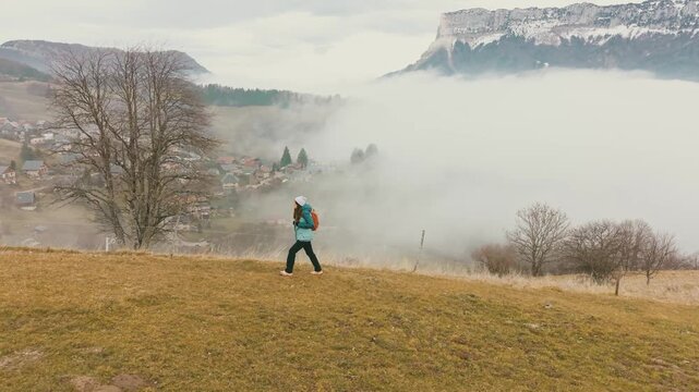 Randonneuse marchant &agrave; travers les prairies du massif de la Chartreuse, en Savoie, avec le majestueux Mont Granier dominant une vall&eacute;e envelopp&eacute;e de brume.