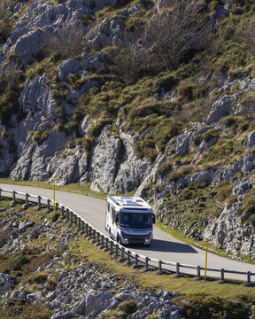 View of a modern motorhome driving along a winding mountain road near the Lakes of Covadonga, surrounded by rocky cliffs and rugged terrain in Asturias, Asturias, Spain.
