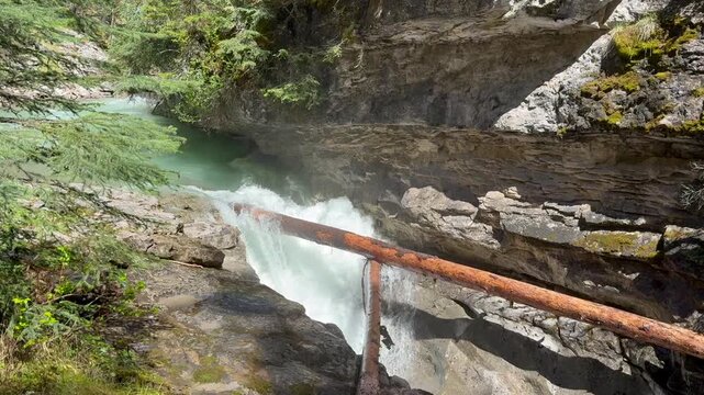 Johnston Creek river in Johnston Canyon in the Banff National Park. British Columbia, Canada. River water flows rapidly over rocks under a wooden bridge surrounded by trees in a natural setting