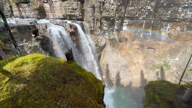 Johnston Creek river in Johnston Canyon in the Banff National Park. British Columbia, Canada. Water flows down a rocky cliff, creating a rainbow above the water in a forested area