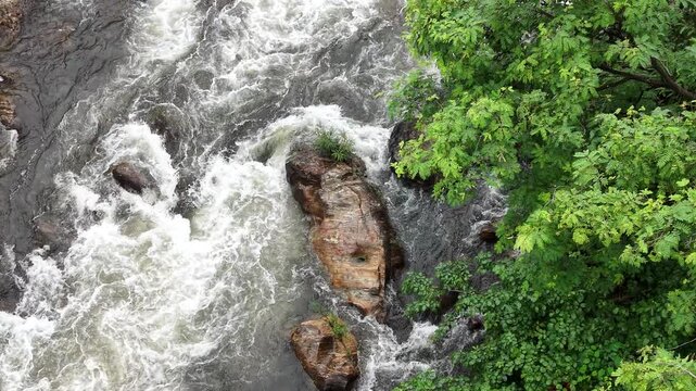 Aerial view of rushing river water flowing over dark rocks surrounded by lush green forest foliage in Maredumilli, Andhra Pradesh, India.