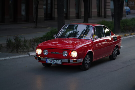 Red Skoda 110 R Coupe classic car front three quarter view driving on city street in dusk with headlights on, Subotica, Serbia, July 4, 2026