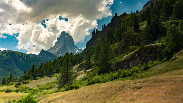 Time lapse of rushing clouds over Matterhorn peak and alpine meadows near Zermatt Switzerland on bright summer day with moving shadows