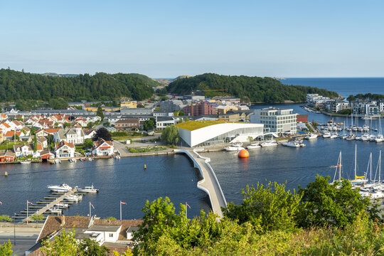 View of the modern building with a green roof and pedestrian bridge spanning the river in the coastal town of Mandal, Agder, Norway.