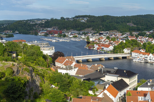 View of the town of Mandal with its river, bridge, and traditional white houses surrounded by lush greenery in Mandal, Agder, Norway.