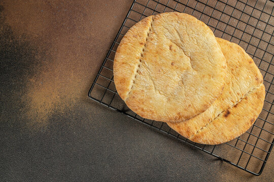 Freshly baked flatbreads resting on a wire cooling rack against a textured brown background, showcasing their golden-brown color and rustic appearance