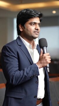 Vertical video: Hearing question, speaker explaining at conference table holding mic in navy blazer