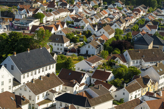 View of the historic town of Mandal with its characteristic white wooden houses, red-tiled roofs, and lush green trees under clear summer light in Mandal, Agder, Norway.