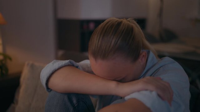 Lonely woman sitting alone at home with her head resting on her knees, looking sad and emotionally exhausted, representing loneliness, stress, worry and difficult feelings.