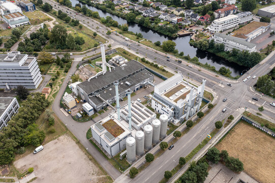 Aerial view of the BTB Heizkraftwerk Adlershof power plant featuring industrial chimneys, storage tanks, and green roofs situated near a canal and urban roads in Berlin, Berlin, Germany.