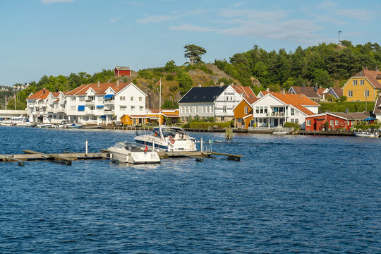 View of the coastal town of Mandal with traditional white and colorful wooden houses along the waterfront and motorboats docked at the pier, Mandal, Agder, Norway.