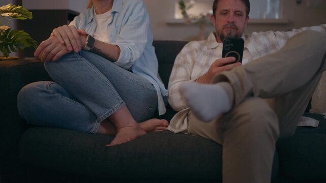Couple sitting on sofa as woman tries to communicate with partner while he remains absorbed in smartphone, illustrating emotional distance, relationship problems and communication issues.
