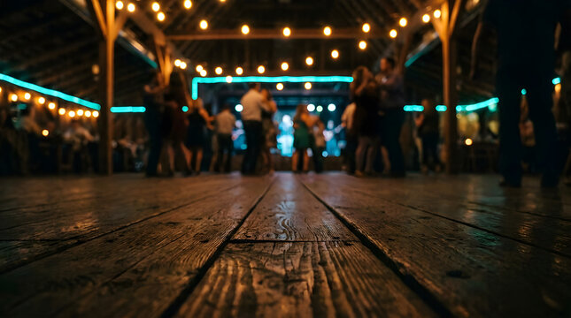 Blurred view of people dancing on a wooden floor in a rustic barn venue with string lights