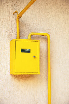 Yellow gas meter box with pipes mounted on an outdoor building wall
