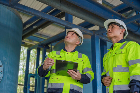 Technician and engineer inspect an overhead industrial pipeline system and record findings at a water processing facility. Concept of engineering, utilities, safety inspection, and plant operations.