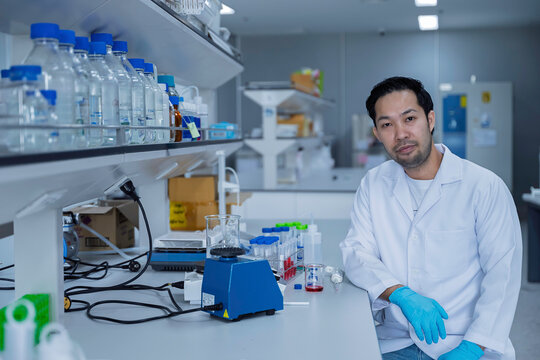 Male researcher looks at the camera while working in a modern scientific laboratory. Concept of research, laboratory science, biotechnology, experiments, analysis, and professional scientist.