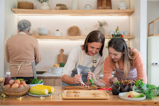 Adult daughter prepares Christmas cookies with her parents in a cozy home kitchen. Concept of family reunion, holiday cooking, festive tradition, homecoming, love, and togetherness.
