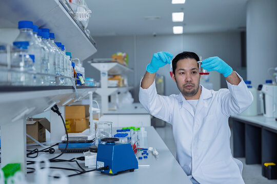 Male researcher looks at the camera while working in a modern scientific laboratory. Concept of research, laboratory science, biotechnology, experiments, analysis, and professional scientist.
