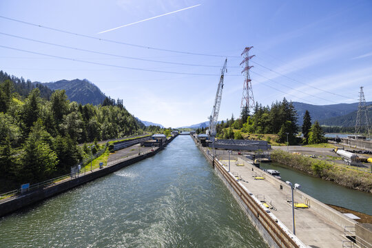 View of the Bonneville Dam on the Columbia River with concrete lock walls, a large crane, power lines, and forested hills in Cascade Locks, Oregon, United States.