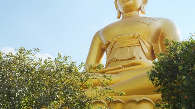 Giant golden buddha statue sitting on lotus base against blue sky with clouds at Wat Paknam Phasi Charoen in Bangkok city, Thailand. Low angle view of Big Seated Buddha. Travel and tourism in Asia