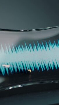 Vertical video: Reacting to audio signal, cyan band forming spikes on curved glass near gold plug