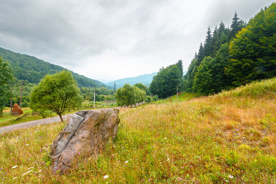 rural landscape. fence near road through field and forest to the high mountains. countryside scenery of ukraine in summer with overcast sky