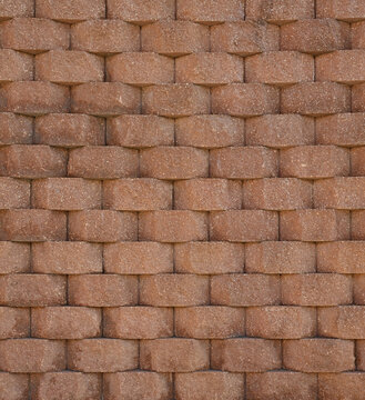 Tapered terra-cotta retaining wall garden blocks in a vertical close-up composition, showing rough textured landscape blocks stacked in a brick wall pattern with visible white aggregate pebbles