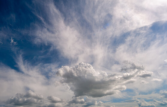 Vibrant blue sky displaying a mix of atmospheric layers, featuring delicate, feathered high-altitude cirrus clouds contrasting with a distinct, puffy white cumulus cloud formation in the lower section