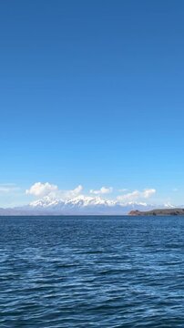 Vista panor&acirc;mica do Lago Titicaca com a Cordilheira Real e picos nevados ao fundo, Bol&iacute;via. Paisagem calma de &aacute;gua e montanhas dos Andes sob c&eacute;u azul.

