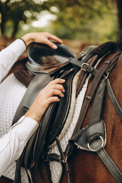 A young woman jockey adjusts the harness on her horse before training.