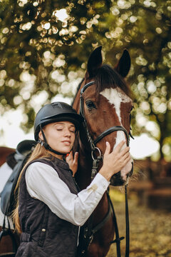 A young female equestrian stands near her horse and prepares for a competition.