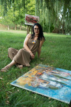 Portrait of an attractive woman artist painter sitting on the grass outdoors