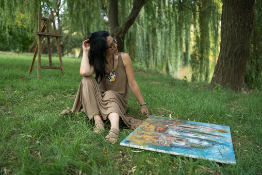 Portrait of an attractive woman artist painter sitting on the grass outdoors