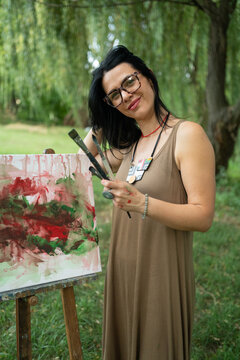 Portrait of a happy woman artist by the canvas outdoors 