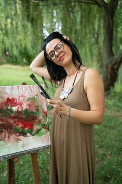 Portrait of a happy woman artist by the canvas outdoors 