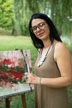 Portrait of a happy woman artist by the canvas outdoors 