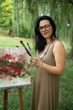Portrait of a happy woman artist by the canvas outdoors 