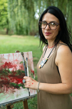 Portrait of a happy woman artist by the canvas outdoors 