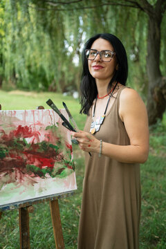 Portrait of a happy woman artist by the canvas outdoors 