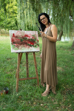 Portrait of a happy woman artist by the canvas outdoors 