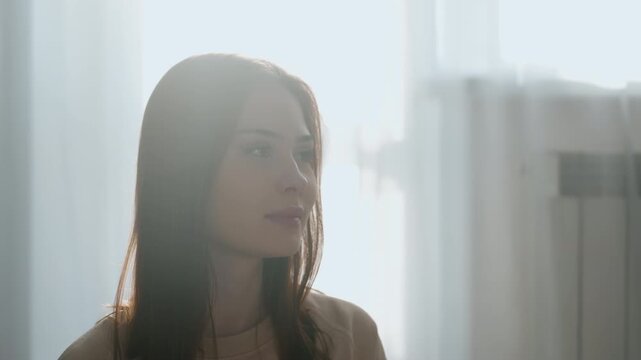 Blue folder reading by caucasian coach, woman holds blue workbook near face then peers over pages with subtle smile, sunlit curtain backdrop, casual sweater and warm morning light, instructional mood