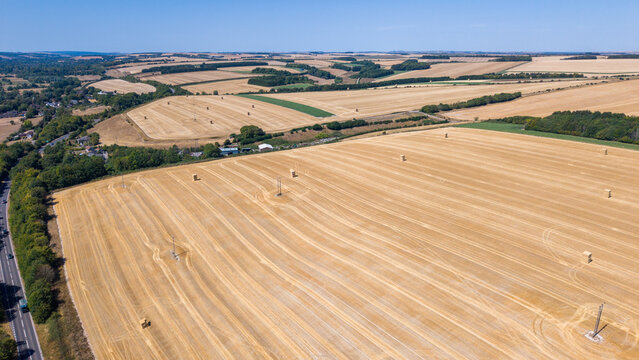 Aerial view of harvested fields with hay bales scattered across the dry arable farmland in the Wiltshire countryside near Salisbury, England, United Kingdom.
