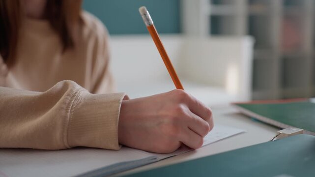 Home study coaching session with pencil and notebook, young woman writing exam practice answers at tidy desk, mentor feedback implied, focused handwriting for grammar drills, lamp glow and sanitizer