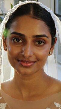 Vertical video: Camera starting, bride turning in lace gown to camera by window, showing veil flare