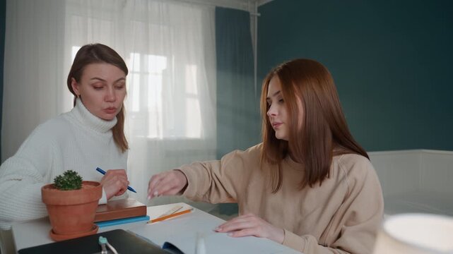 Two white women tutoring at home private tutor guiding student through grammar exercises with pen and notebook on desk plant on table cozy livingroom natural daylight collaborative study correction