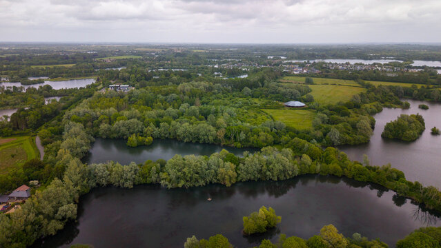 Aerial view of the Coate Water nature reserve featuring interconnected lakes, lush woodland, and expansive meadows, Swindon, England, United Kingdom.