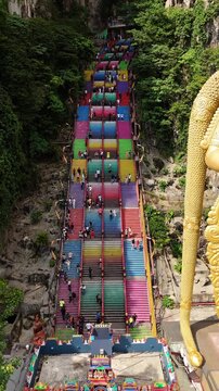 Aerial view of colorful stairs at Batu Caves with visitors climbing the steep steps surrounded by lush greenery in Kuala Lumpur, Federal Territory of, Malaysia.